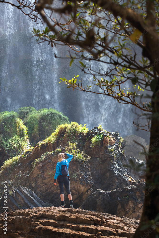 Obraz premium Tourist traveler standing on a rock, hiker looking to a Elephant Waterfall below in trip in Vietnam, woman enjoying nature