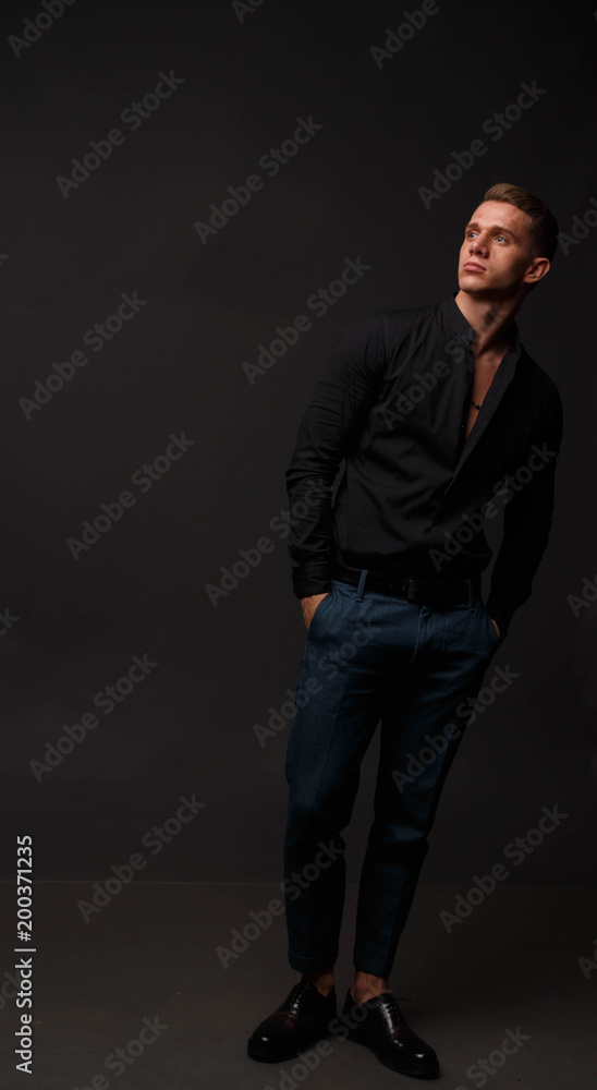 attractive white man in black shirt and blue pants stands on a dark background attractive white man in black shirt and blue pants stands on a dark background