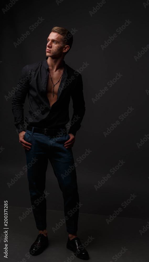 attractive white man in black shirt and blue pants stands on a dark background attractive white man in black shirt and blue pants stands on a dark background