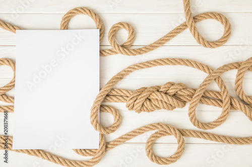 top view of empty paper on brown nautical knotted ropes on white wooden surface