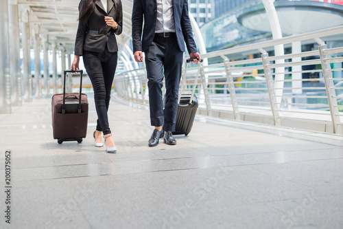 business man and businesswoman wear black suit walk together with luggage on the public street, business travel concept
