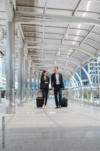 business man and business woman wear black suit walk together with luggage on the public street, business travel concept