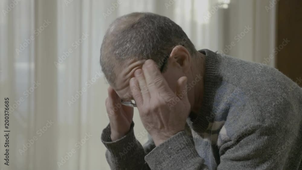 Closeup of stressed elderly man suffering from migraine massaging his temples and forehead healing the pain Closeup of stressed elderly man suffering from migraine massaging his temples and forehead healing the pain