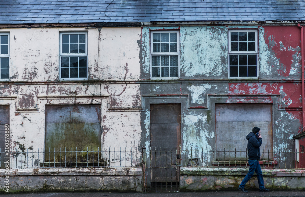 Man walking by abandoned and boarded up buildings on Carrigrohane Rd in Cork city, Ireland