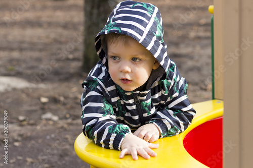Portrait of thoughtful little boy playing outside in the playground, adorable toddler in a hood playing outdoors. photo