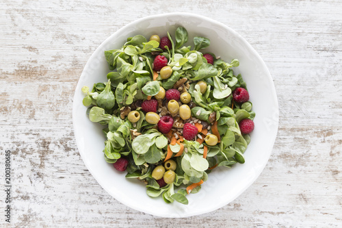 Salad of canons, raspberries, raisins, olives, nuts, carrots and pips on white wooden background