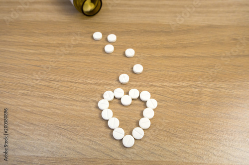 Tablets scattered from a jar in the shape of a heart on a light wooden table close up