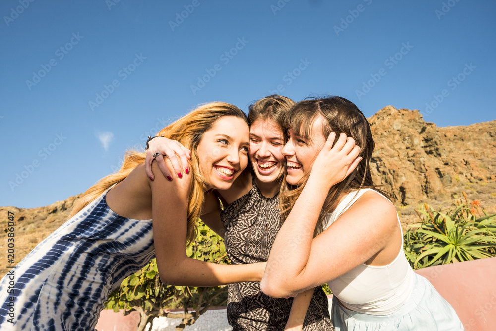 three young women hug themselves in a sunny day.