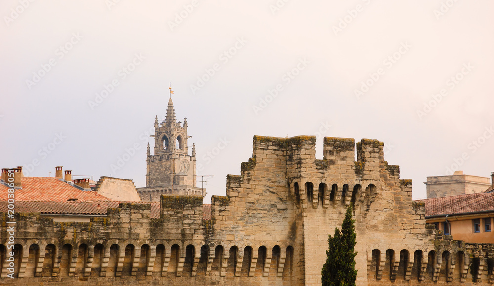 Cityscape of medieval Avignon with fortified walls and clock tower. Evening dusk.