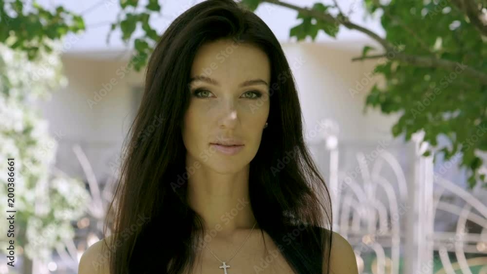 Portrait of pretty young woman with straight dark hair smiling, looking at camera on the summer street. Slow motion. HD Portrait of pretty young woman with straight dark hair smiling, looking at camera on the summer street. Slow motion. HD