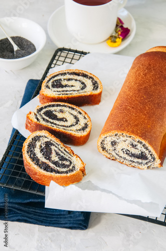 Traditional polish festive pastry - Makowiec- Poppy seed roll served on a wire rack. White stone background.