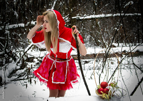 A girl in a red dress in a winter forest makes her way through the thickets. Little Red Riding Hood.