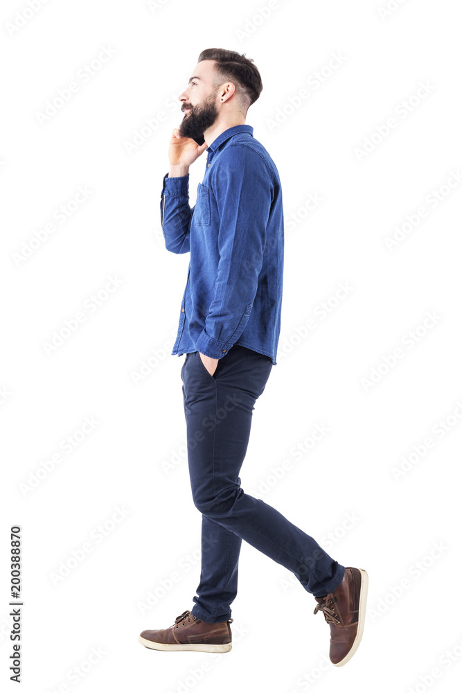 Happy confident successful business man walking and talking on cell phone with hands in pockets looking up. Full body isolated on white background. Happy confident successful business man walking and talking on cell phone with hands in pockets looking up. Full body isolated on white background.