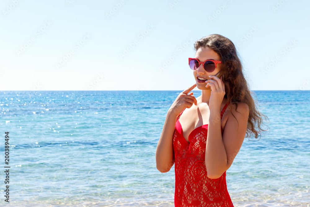 Happy smiling girls using mobile smart phone on the beach. girl is talking on the mobile phone by the sea Happy smiling girls using mobile smart phone on the beach. girl is talking on the mobile phone by the sea