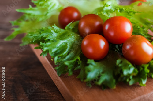 Cherry tomatoes and salad leaves on the cutting board with soft focus on the background. Top view. Copy text space. 