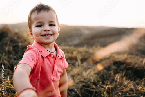 portret of a beautiful young mother in a long red dress with her little son walking on mountain sites on the sunset in summer, dry grass.Mom holds her son's hand and hugs