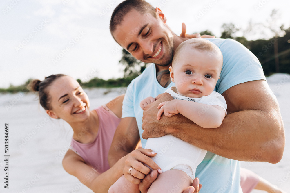 Happy emotional family: mother, father holds little baby boy on sunset Happy emotional family: mother, father holds little baby boy on sunset