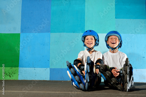 Yong little athletic boys on roller sitting against the blue graffiti wall