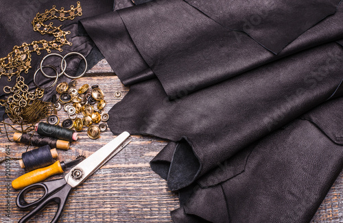 Black leather texture, rivets, buttons, scissors, threads on wooden background, surface
