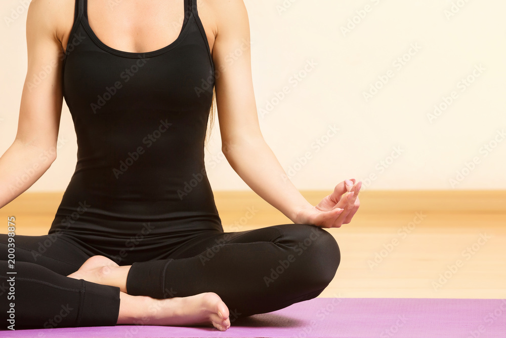 Closeup image of female sitting in lotus pose and meditating at gym.