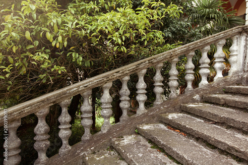 beautiful abandoned staircase with a handrail of stone on a background of green leaves