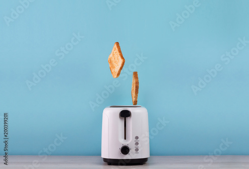 Foto Roasted toast bread popping up of stainless steel toaster on a blue backgroun