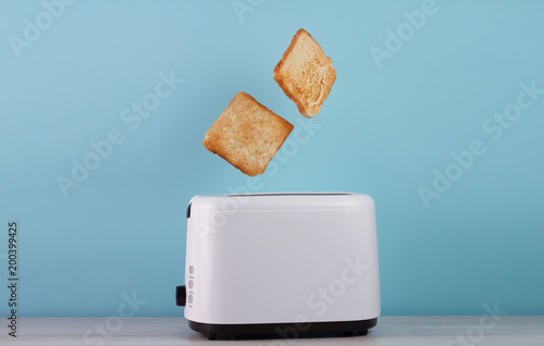 Roasted toast bread popping up of stainless steel toaster on a blue backgroun.