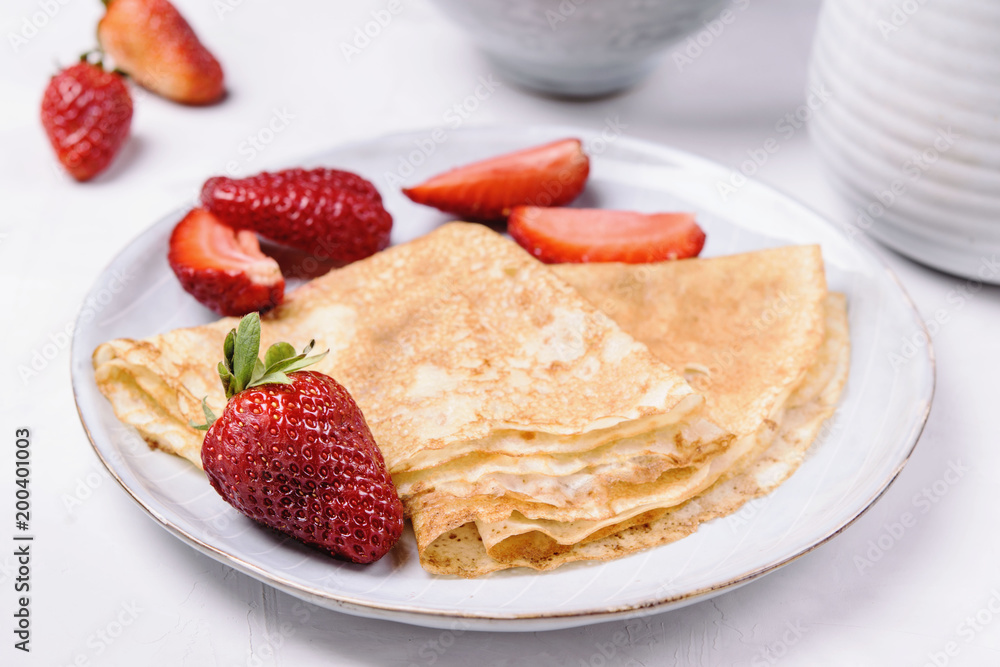 Openwork thin cheese crepes served with strawberry on grey concrete background. Homemade pancakes. Delicious breakfast