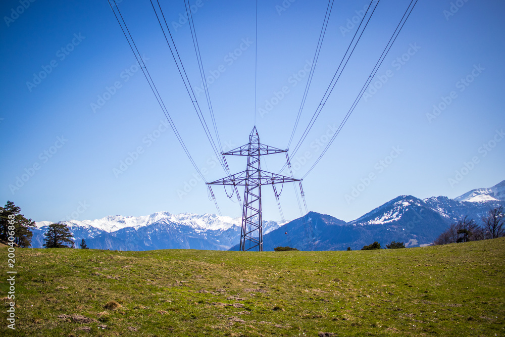 Strommast auf einem Berg inmitten der Schweizer Alpen mit grüner Wiese und blauem Himmel