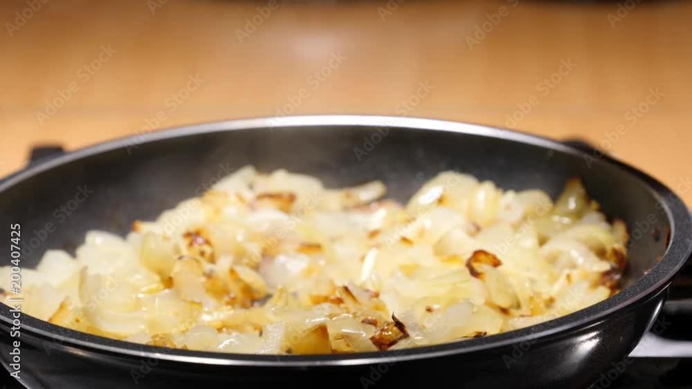 Chopped onions fried in hot frying pan, hand mixing with wooden spoon spatula. Vegetable preparing, meals with vegetables. Slow motion Chopped onions fried in hot frying pan, hand mixing with wooden spoon spatula. Vegetable preparing, meals with vegetables. Slow motion