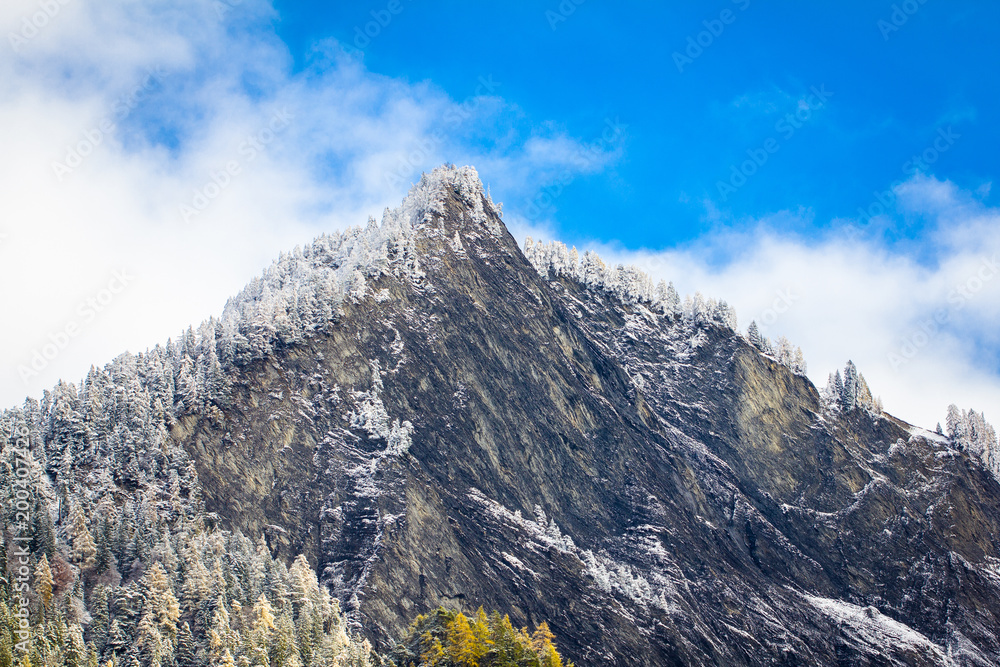 massive Bergspitze in der Schweiz im Winter, schneebedeckt, mit verschneiten Bäumen im Wald und blauer Himmel mit ein wenig Wolken