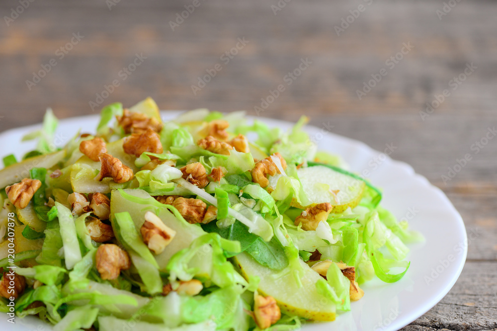 Pear cabbage slaw recipe. Simple salad with raw pear, cabbage and walnuts on a plate. Rustic wooden background. Clean eating. Closeup Pear cabbage slaw recipe. Simple salad with raw pear, cabbage and walnuts on a plate. Rustic wooden background. Clean eating. Closeup