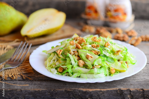 Pear and cabbage salad. Homemade salad with pear, cabbage and walnuts on a plate. Rustic wooden background. Quick healthy food. Closeup