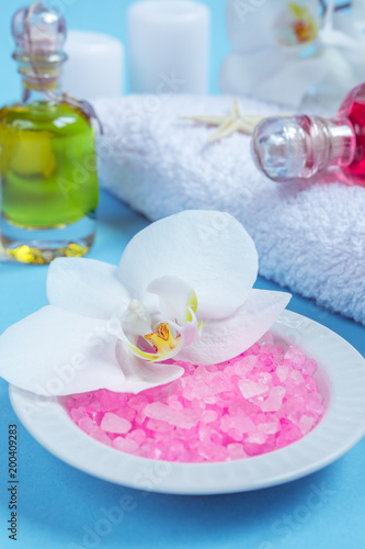 Spa background, flat layout with pink sea salt, candles and aroma oils and beauty care products on a blue background