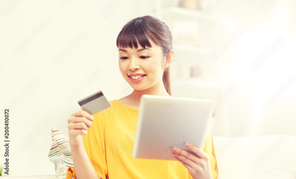 people, internet bank, online shopping, technology and e-money concept - happy asian young woman sitting on sofa with tablet pc computer and credit card at home people, internet bank, online shopping, technology and e-money concept - happy asian young woman sitting on sofa with tablet pc computer and credit card at home
