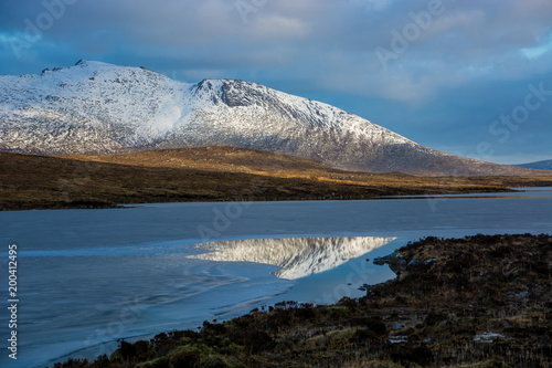 Reflection of mountain peak covered by snow in frozen lake at Arran island, Scotland