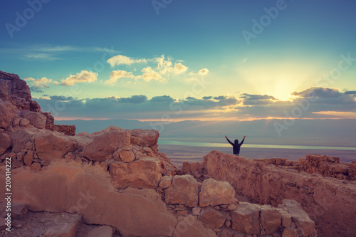 Wallpaper Mural Sunrise over Masada fortress. Silhouette of man with hands in the air looking at magical sunset.  Israel Torontodigital.ca