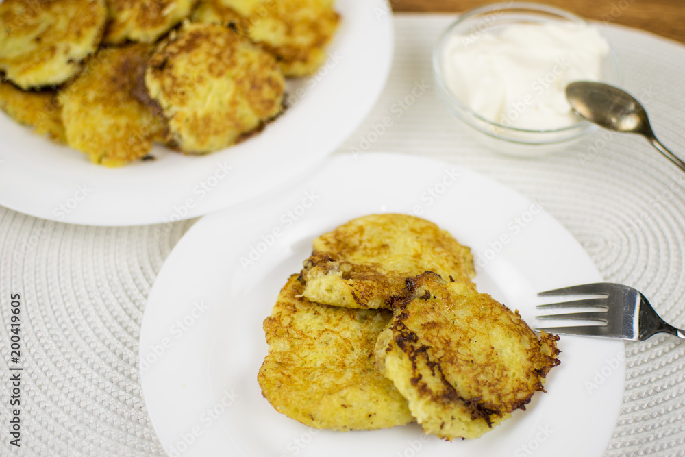 Fried potato pancakes on a white plate and sour cream. Fried potato pancakes on a white plate and sour cream.