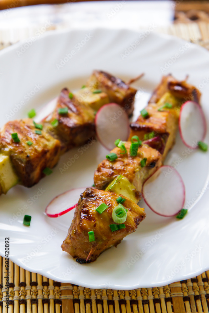 Skewers of pork, radishes and green onions on a white plate side view