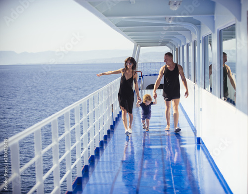 Happy family with cute son on summer vacation. Family travelling on cruise ship on sunny day. Family rest concept. Father, mother and child walk on deck of cruise liner with sea on background.