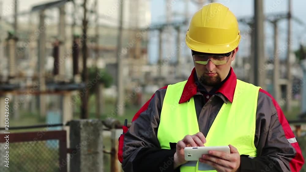 Worker at electric power plant uses smartphone. Power engineering specialist with cell phone in hand on electric power station Worker at electric power plant uses smartphone. Power engineering specialist with cell phone in hand on electric power station