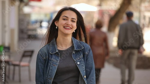 Portrait of a stylish young woman with an irresistable smile and long loose hair who laughs open-heartedly in an alley on a sunny day in spring