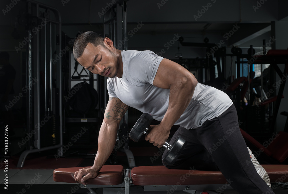 Muscular builder man training his body with dumbbell in Modern fitness center Muscular builder man training his body with dumbbell in Modern fitness center