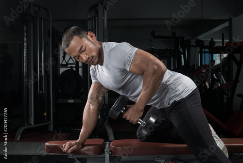 Muscular builder man training his body with dumbbell in Modern fitness center