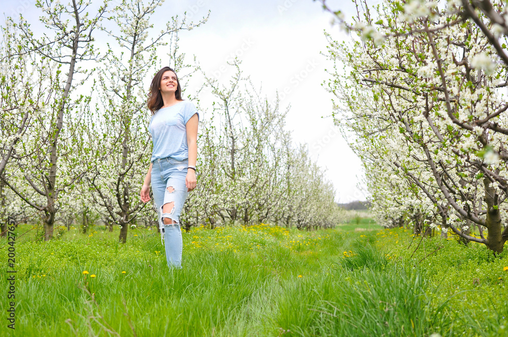 Beautiful young woman walking in blooming orchard. Happy girl in spring time in nature