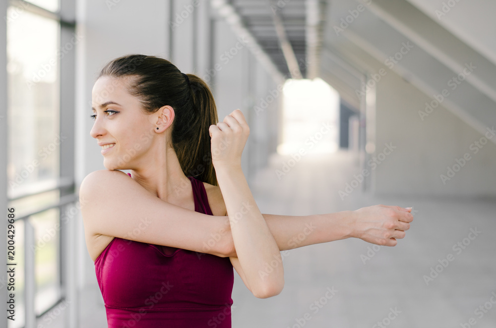 Active young woman warming up and stretching arms and shoulders