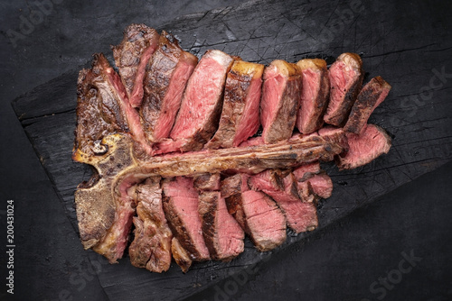 Barbecue dry aged wagyu porterhouse steak sliced as top view on a burnt board