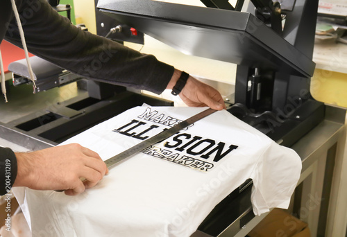 Canvas Print Young man printing on t-shirt at workshop