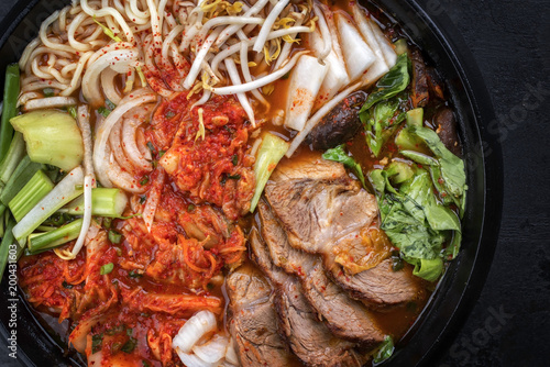 Traditional Korean kimchi jjigae with grilled pork belly and ramen as top view in a pot
