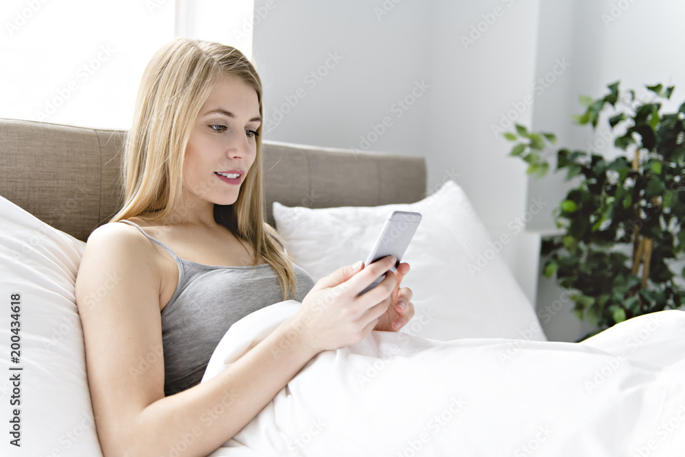 Beautiful young woman on bed, 20s year old using cellphone